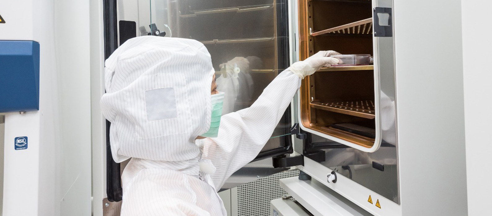 pessoa com epi de proteção biológica colocando uma placa de petri em uma incubadora de co2